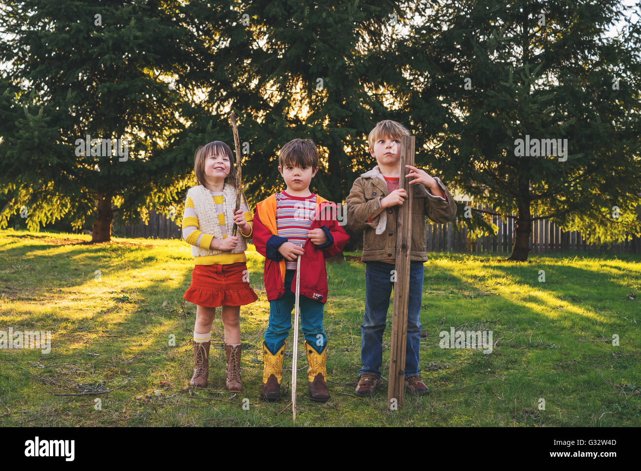 Drei Kinder stehen im Garten halten Stöcke Stockfoto
