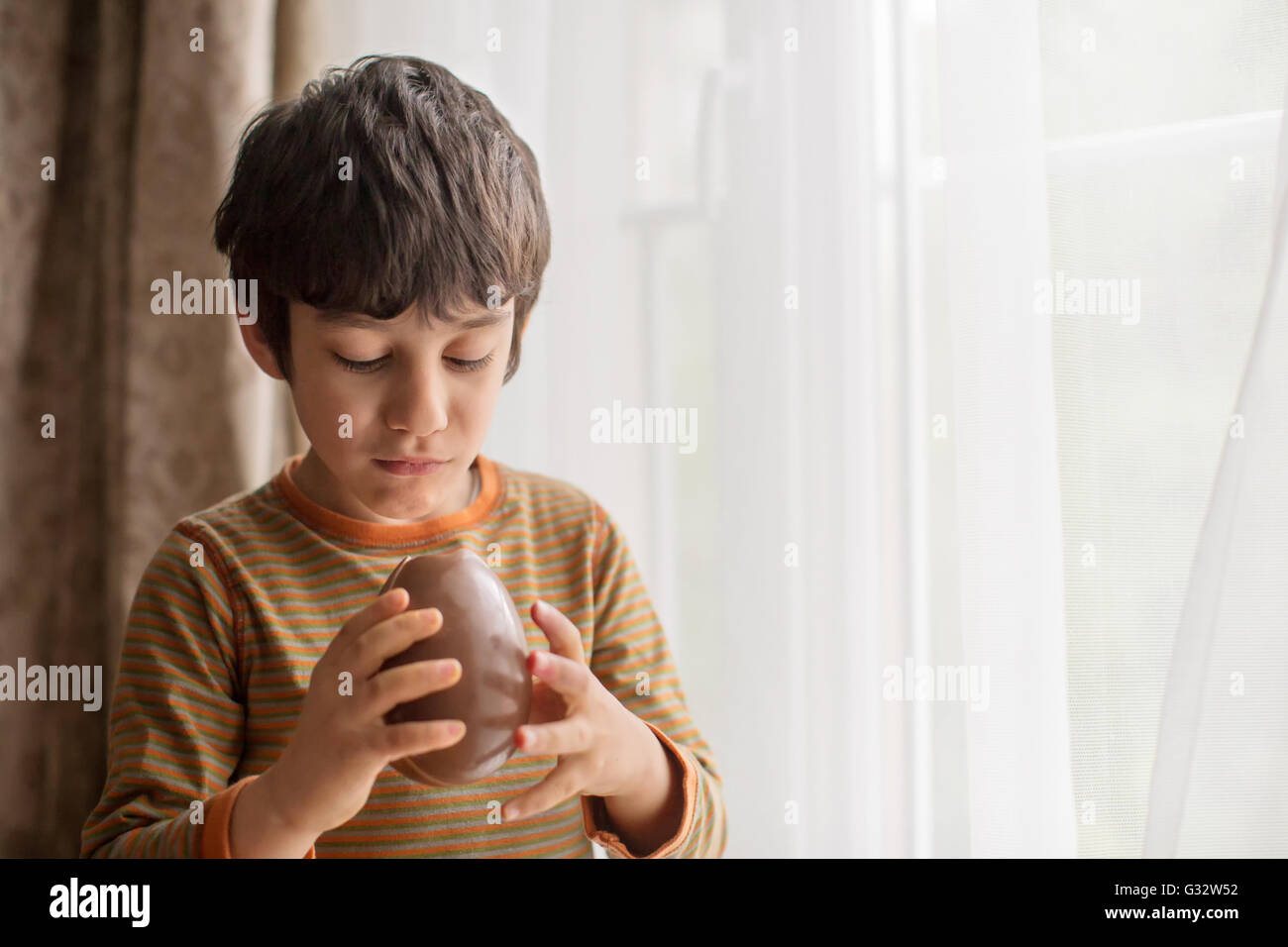 Junge stand Fenster Essen eine große Schokoladen Osterei Stockfoto