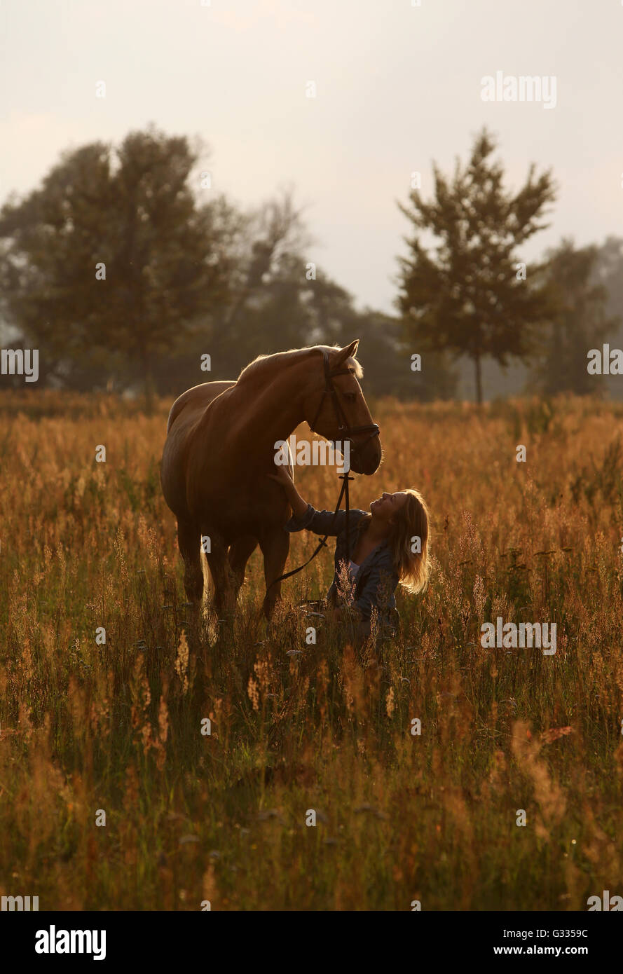 Brieselang, Deutschland, Mädchen kauert auf einer Wiese auf ihr Pferd und betrachtet ihn liebevoll Stockfoto