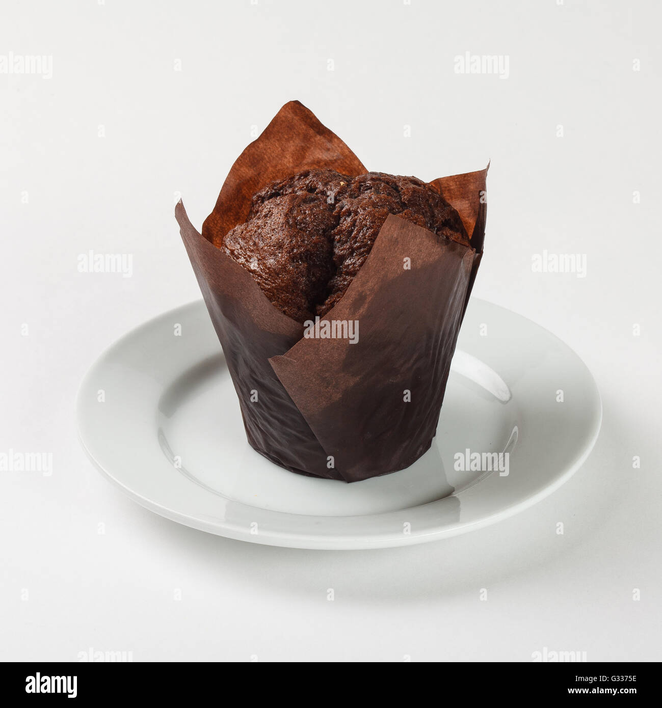 Leckere Schoko-Muffin Kuchen in braunem Papier auf die Platte auf weißem Hintergrund. Schließen Sie die Seitenansicht. Stockfoto