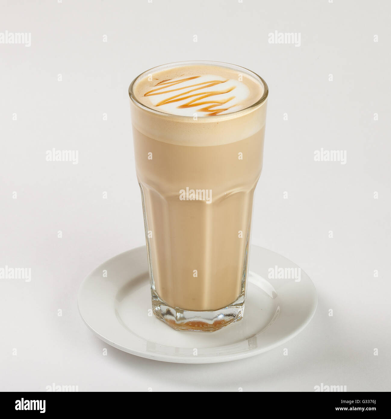 Leckeren Latte in ein hohes Glas auf dem Teller auf weißem Hintergrund. Schließen Sie die Seitenansicht. Stockfoto