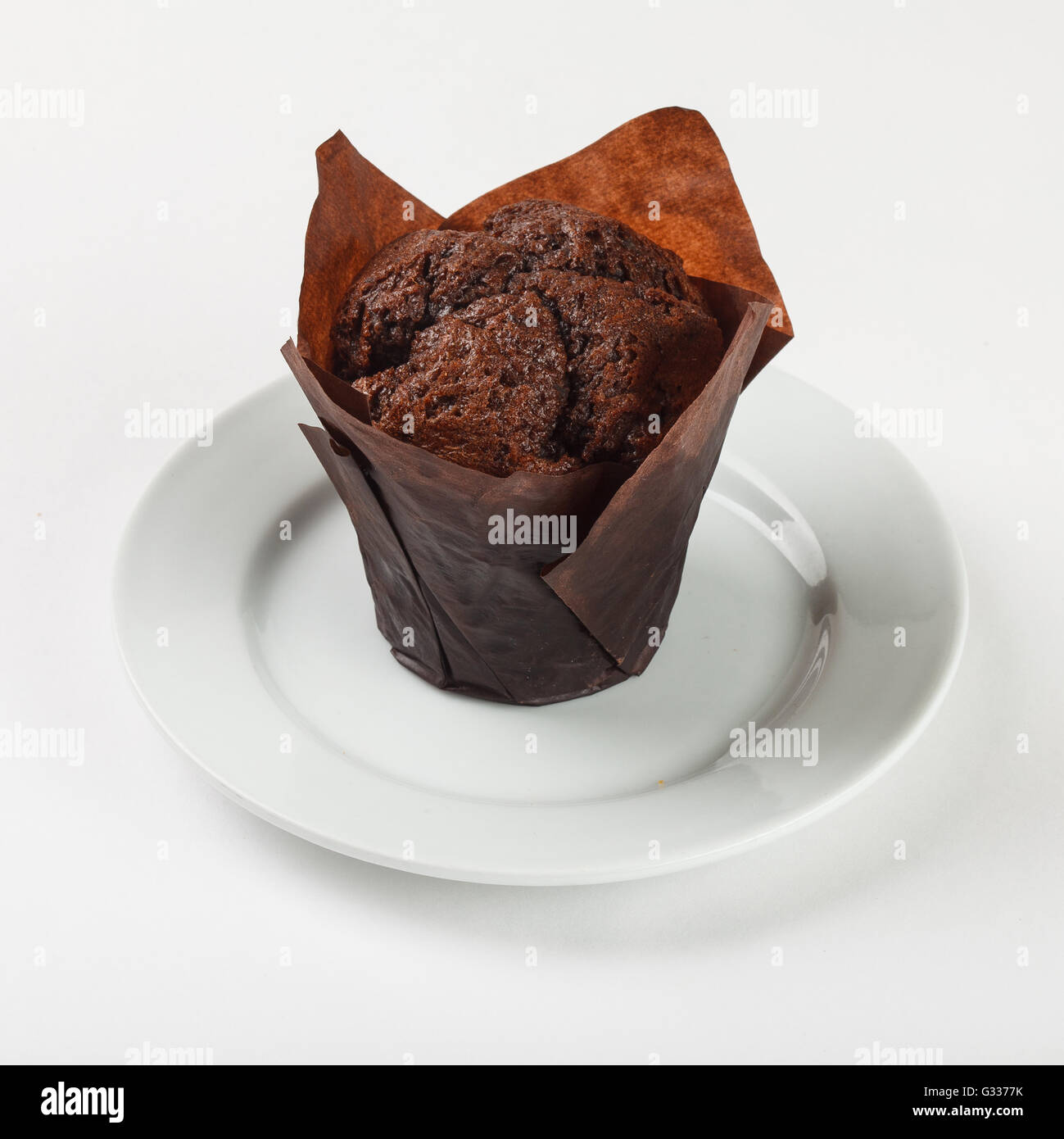 Leckere Schoko-Muffin Kuchen in braunem Papier auf die Platte auf weißem Hintergrund. Schließen Sie die Seitenansicht. Stockfoto