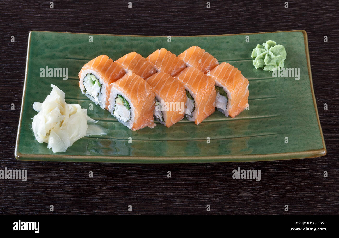 Sushi-Rollen auf einem Teller mit Lachs auf dunklen braunen Holztisch. Seitenansicht. Stockfoto