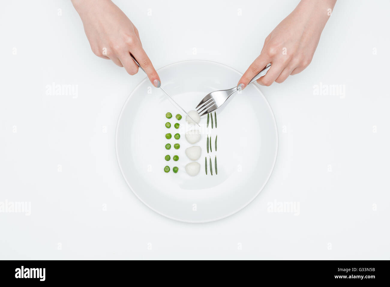 Draufsicht der Hände der jungen Frau Essen, grüne Erbsen, Mozzarella und Kräutern mit Messer und Gabel auf weißem Hintergrund Stockfoto