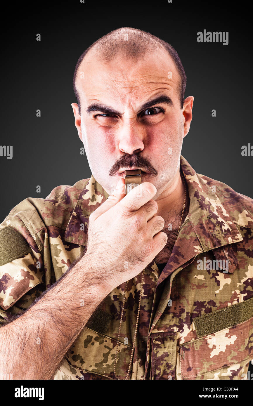 ein Soldat oder Drill Sergeant weht eine Pfeife über einen dunklen Hintergrund Stockfoto