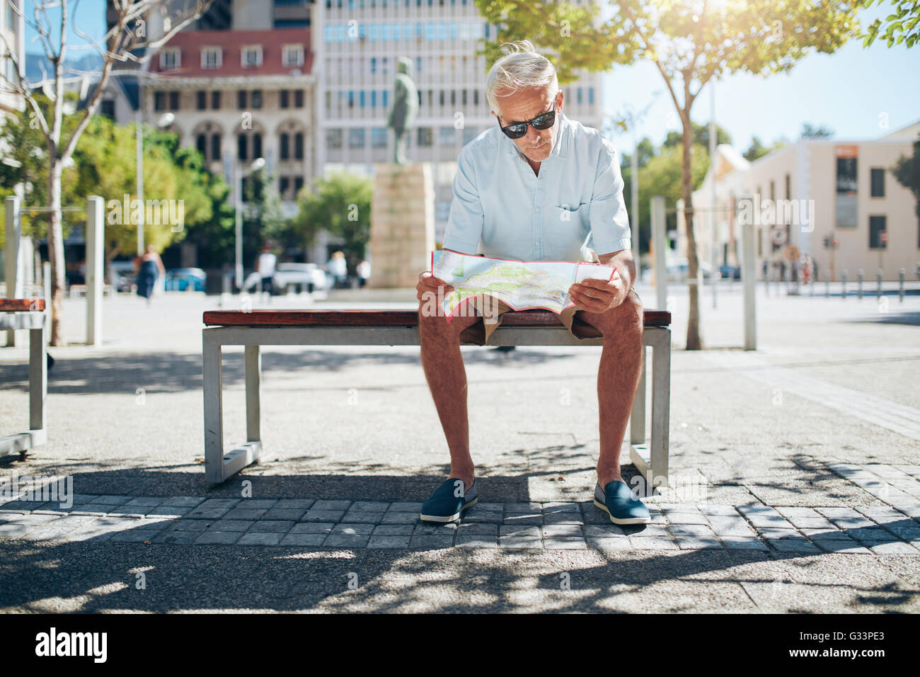 Senior männlichen Touristen sitzen auf einer Bank und auf der Suche nach einem Ort auf der Karte. Reifer Mann sitzen im Freien in der Stadt und lesen ein Stockfoto