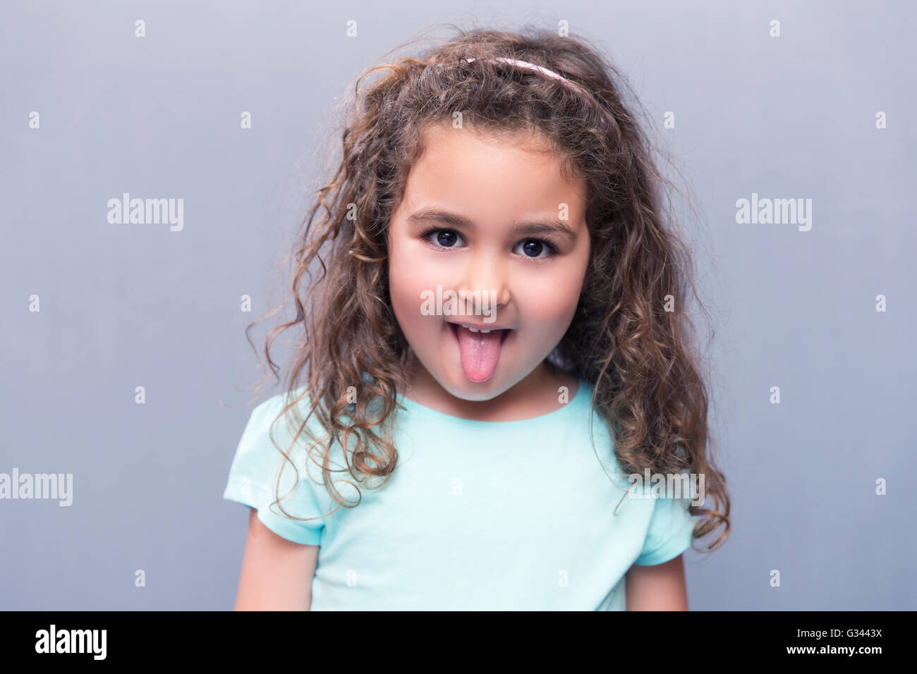 Porträt der kleine süße Mädchen mit dem lockigen Haar zeigt Zunge in die Kamera. Studio gedreht Stockfoto
