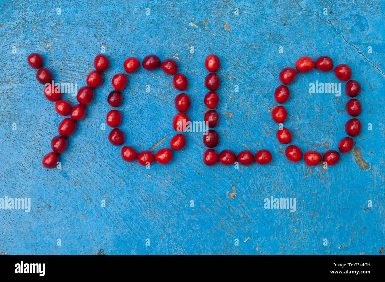 Kirschen, angeordnet, um das Wort YOLO auf strukturierten blauen Hintergrund bilden Stockfoto
