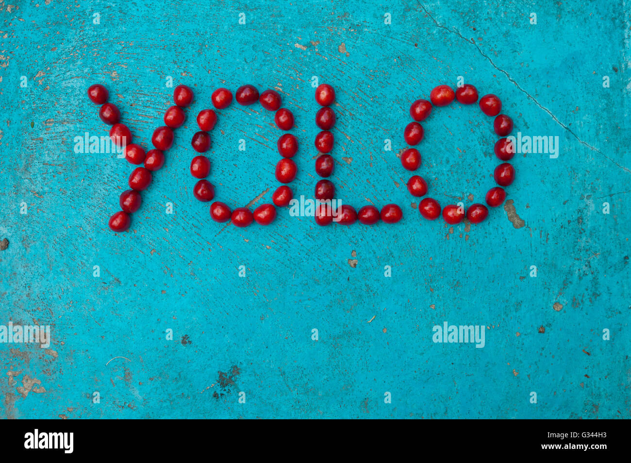 Kirschen, angeordnet, um das Wort YOLO auf strukturierten blauen Hintergrund bilden Stockfoto