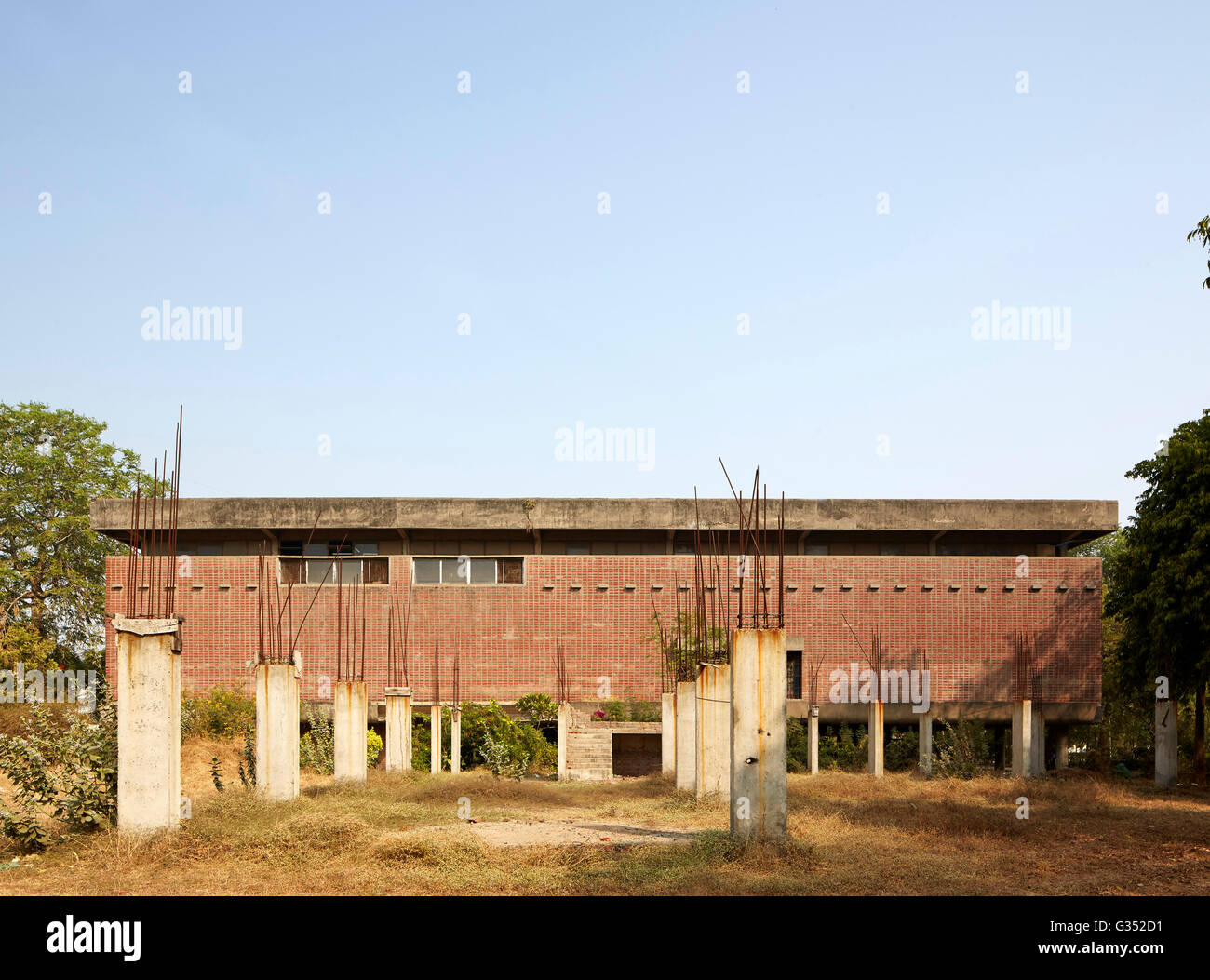 Blick von der Straße mit verlassenen Baustelle im Vordergrund. Sanskar Kendra, Ahmedabad, Indien. Architekt: Le Corbusier, 1951. Stockfoto