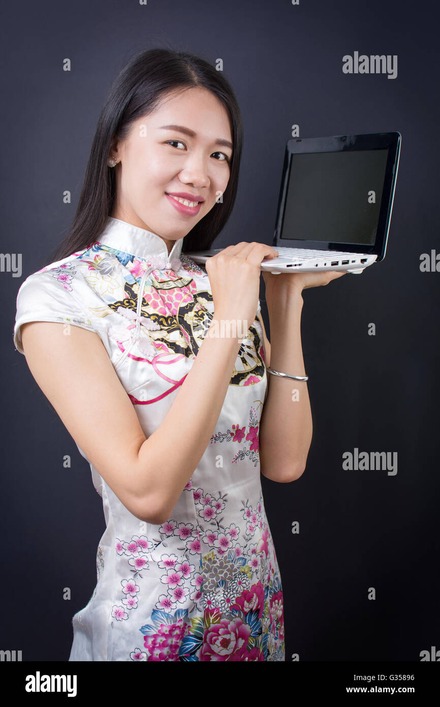 Junge asiatische Frau hält einen Laptop mit chinesischen Kleid Stockfoto