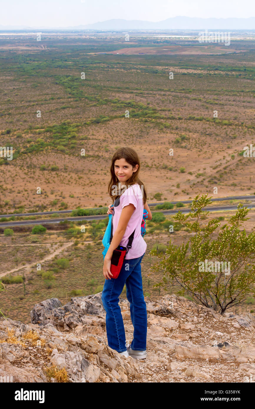 Ein junges Mädchen, das selbstbewusst und stolz auf ihre Leistung sieht, steht an der Spitze eines kleinen Berges, die sie bestiegen hat. Stockfoto
