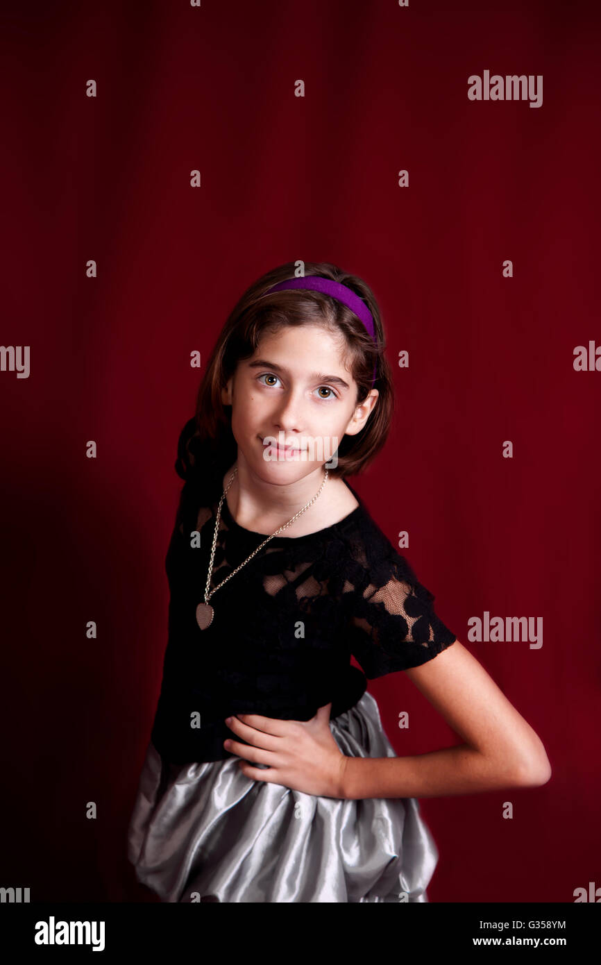 Studio-Porträt eines jungen Tween Mädchen auf einem roten Hintergrund.  Sie lehnt sich selbstbewusst in Richtung der Kamera mit einem wissenden Ausdruck. Stockfoto