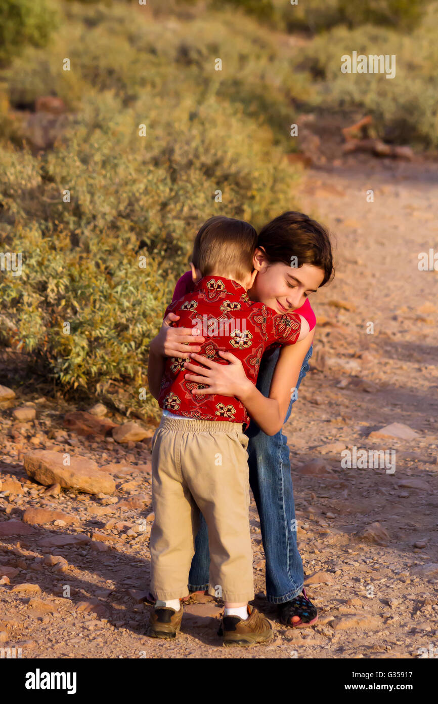 Eine große Schwester gibt ihren kleinen Bruder eine tröstliche Umarmung, wenn er müde, auf einem einsamen Wanderweg wird. Stockfoto