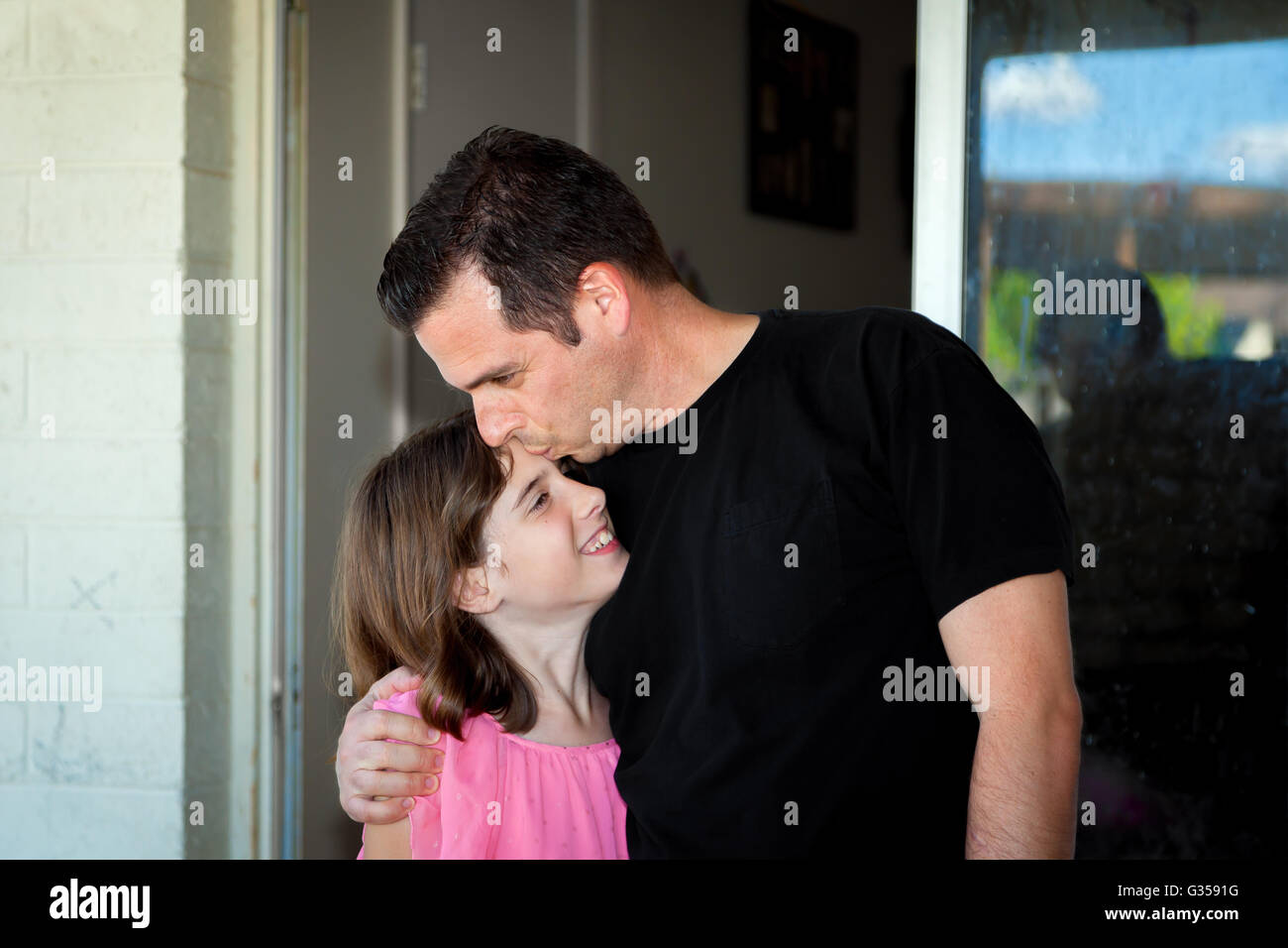 Ein Vater küsst seine Tochter auf die Stirn, als er sie umarmt und sie in der Nähe zieht. Stockfoto