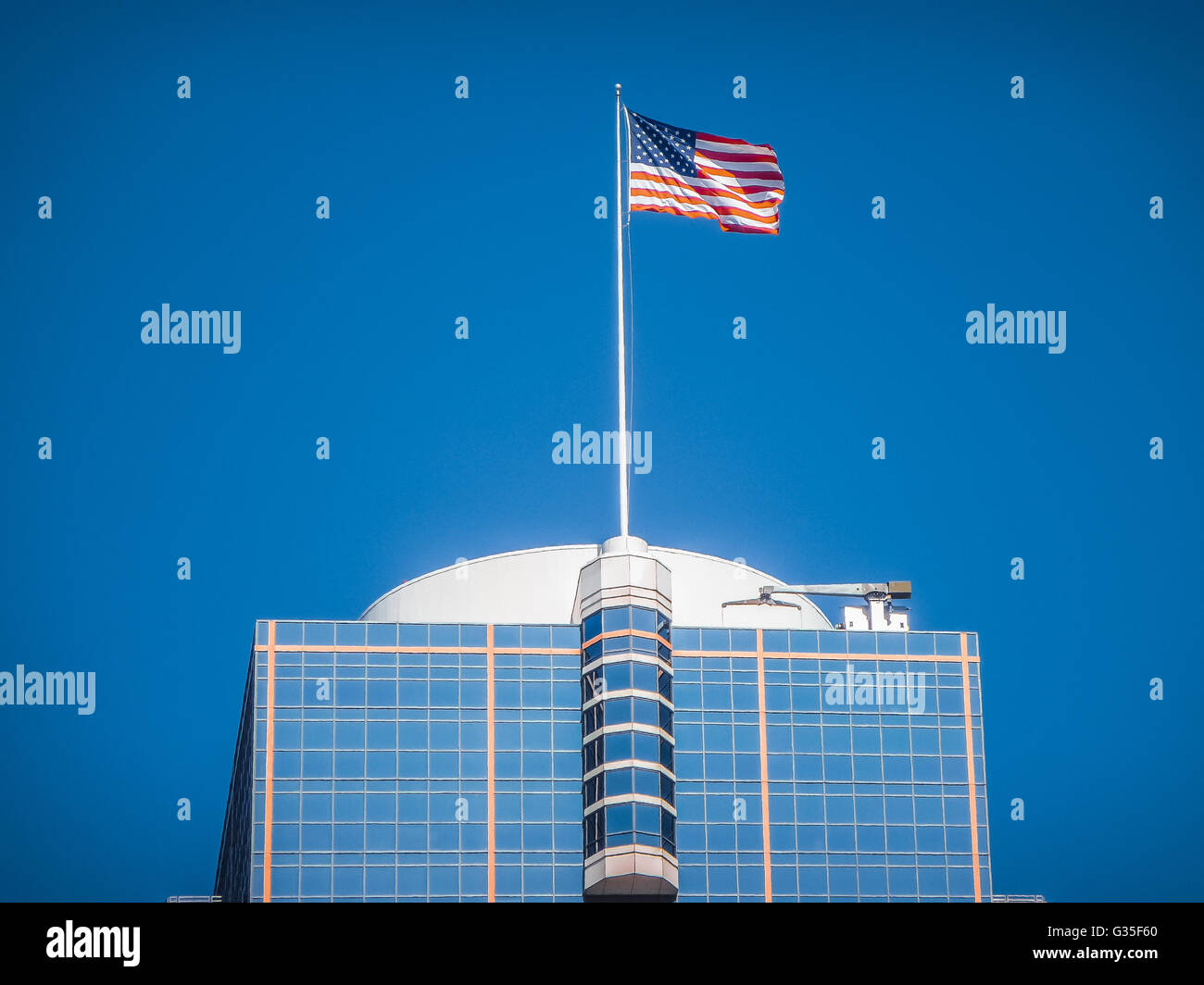 Amerikanische Flagge winken zusätzlich zu einem modernen Wolkenkratzer hoch in der Luft an einem sonnigen Tag gegen den blauen Himmel Stockfoto