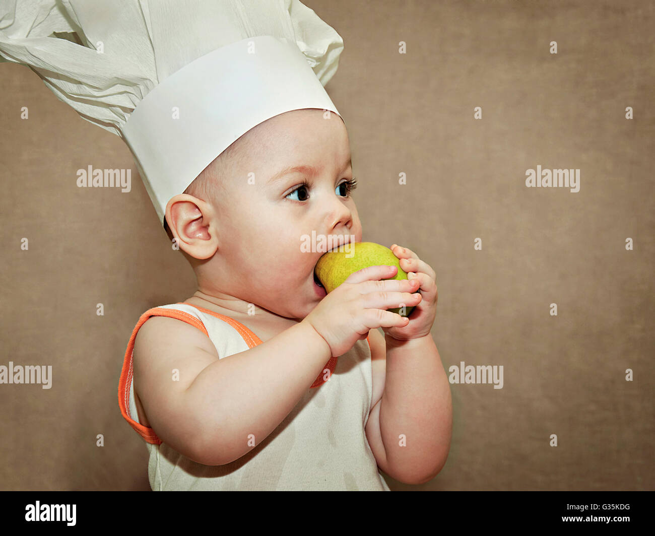 kleines Baby in eine Kochmütze Essen eine Birne Stockfoto