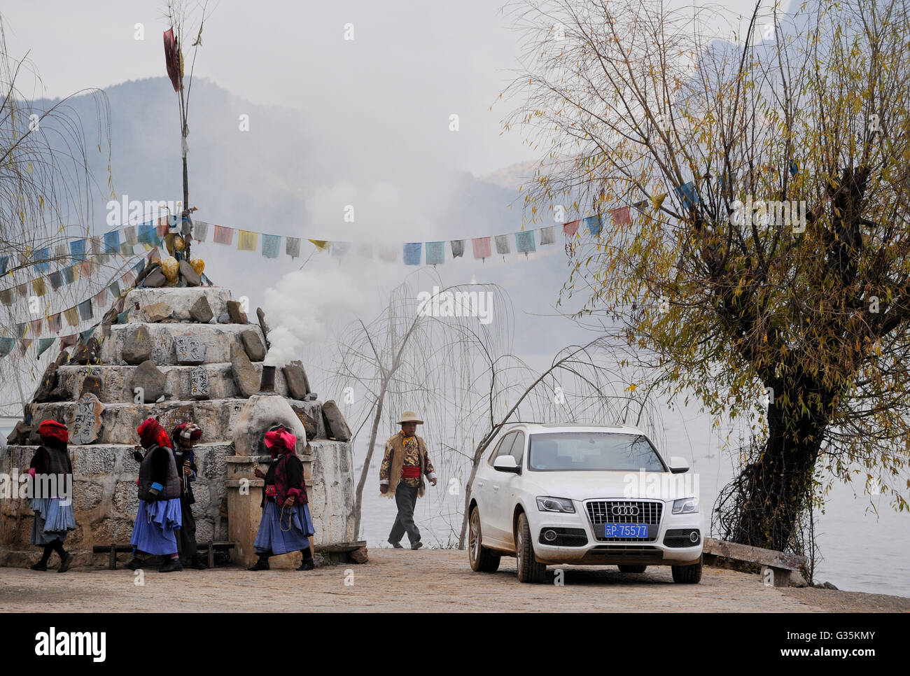 CHINA Yunnan, Lugu Lake Mosuo, die ethnischen Minderheiten angehören, die buddhistischen und Frauen haben eine Matriarchin, buddhistische Mosuo Frauen mit Gebet Mühle Surround buddhistischen Schrein am Lugu See, von einer pipe Räucherstäbchen Rauch steigt, neben weißen Audi Auto mit chinesischen Nummernschild Stockfoto