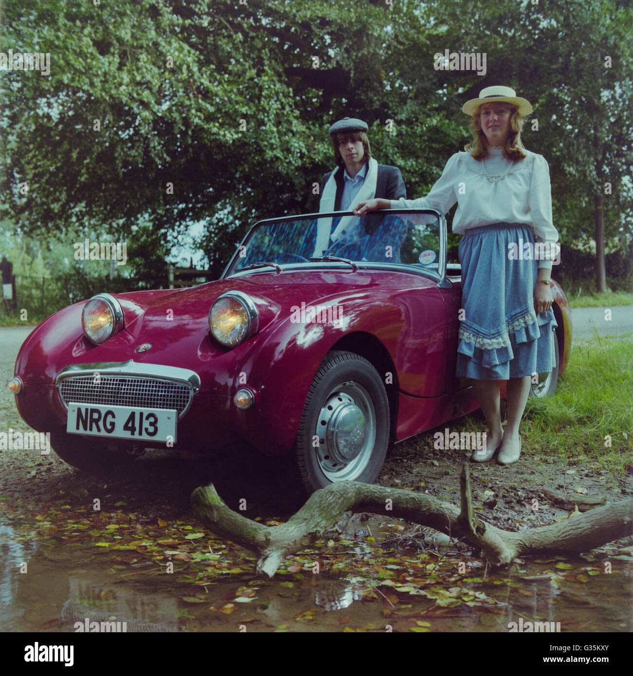 Archivbild eines kastanienbraunen Austin-Healey Sprite Frogeye-Sportwagens NRG 413 aus dem Jahr 1959 mit Fahrer und Beifahrer in zeitlicher Kleidung, Lincolnshire, 1983. Ab 2022 ist dieses Fahrzeug weiß und auf SORN. Stockfoto