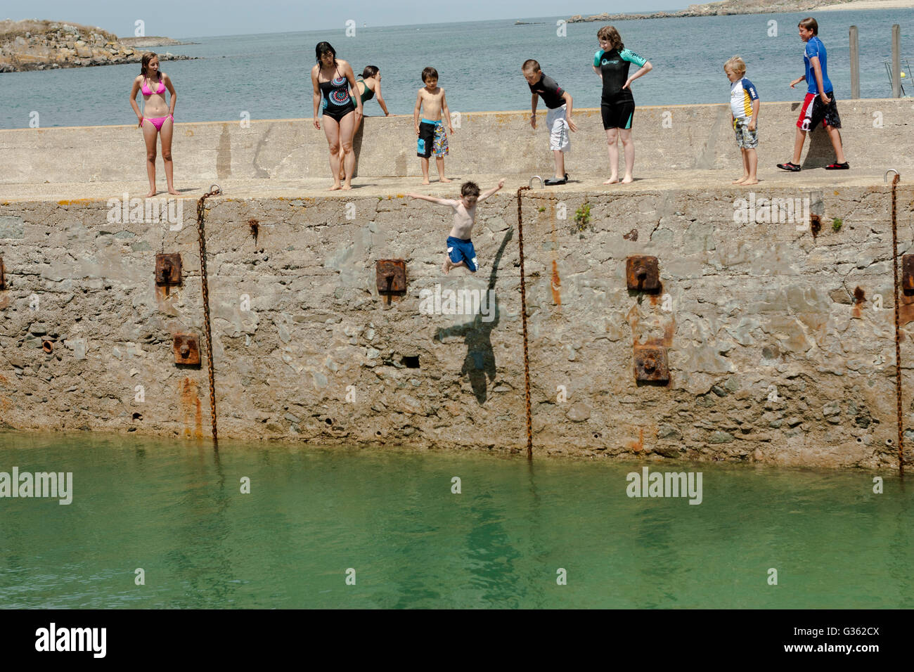 Jungen und Mädchen springen vom Steg ins Meer im Hafen von Herm Island, Kanalinseln Stockfoto