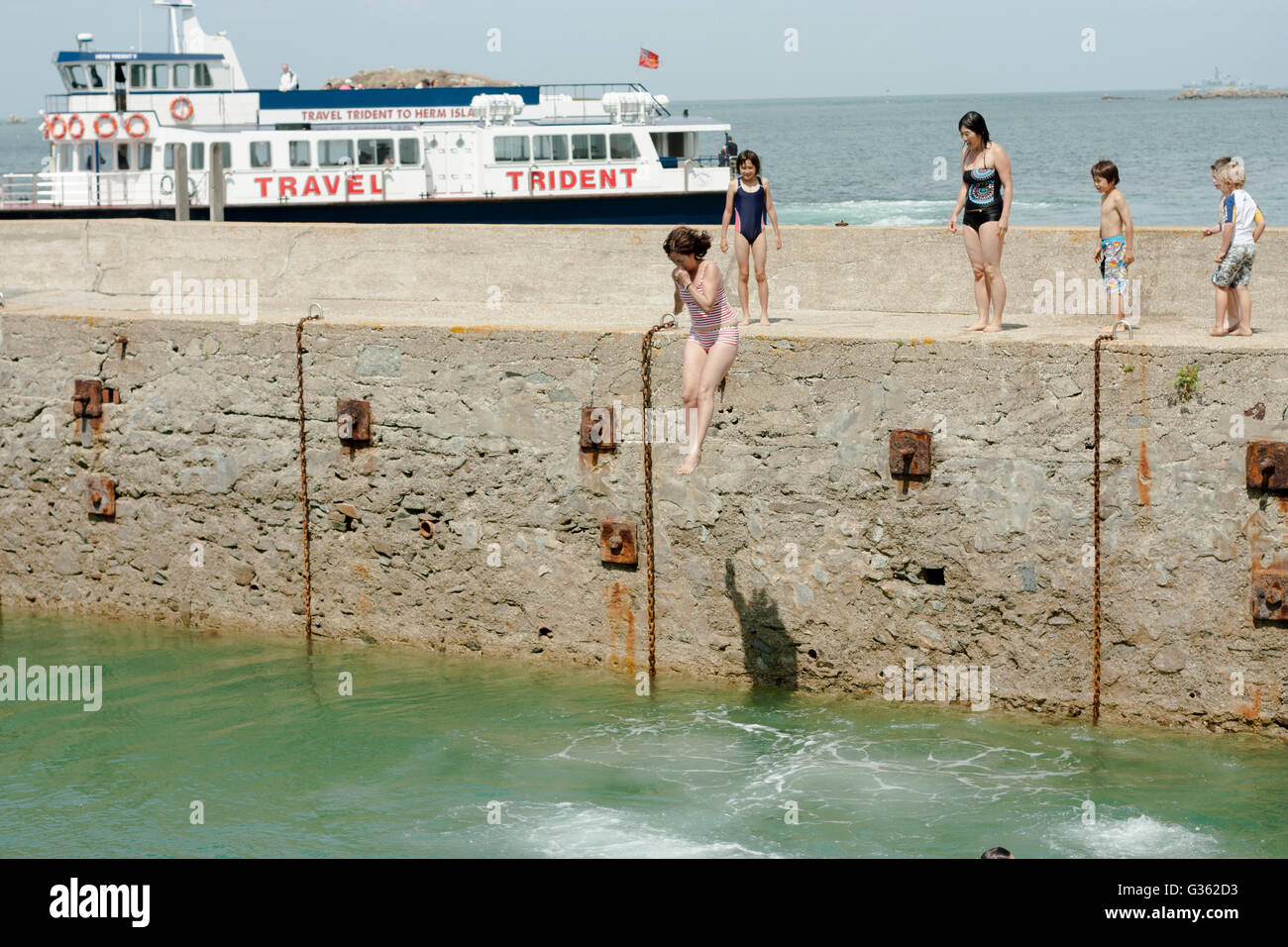 Jungen und Mädchen springen vom Steg ins Meer im Hafen von Herm Island, Kanalinseln Stockfoto