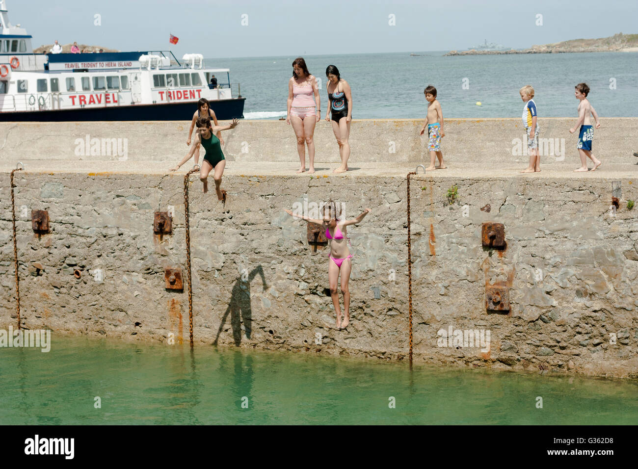 Jungen und Mädchen springen vom Steg ins Meer im Hafen von Herm Island, Kanalinseln Stockfoto
