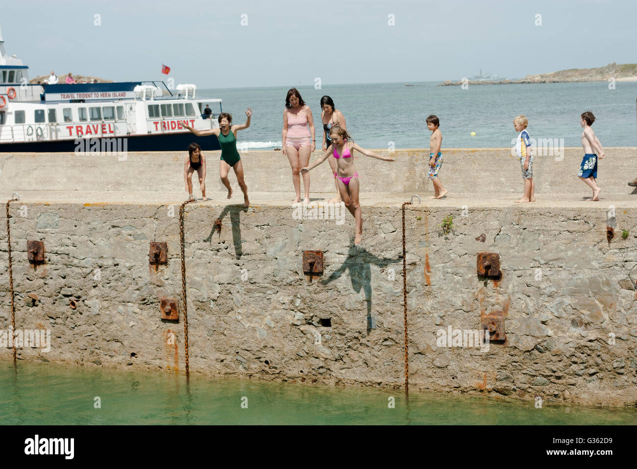Jungen und Mädchen springen vom Steg ins Meer im Hafen von Herm Island, Kanalinseln Stockfoto