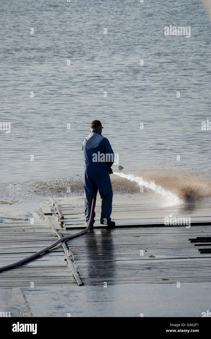 Ein Mann mit einem Wasserschlauch waschen Sie eine Slipanlage an Upnor, Kent. Stockfoto