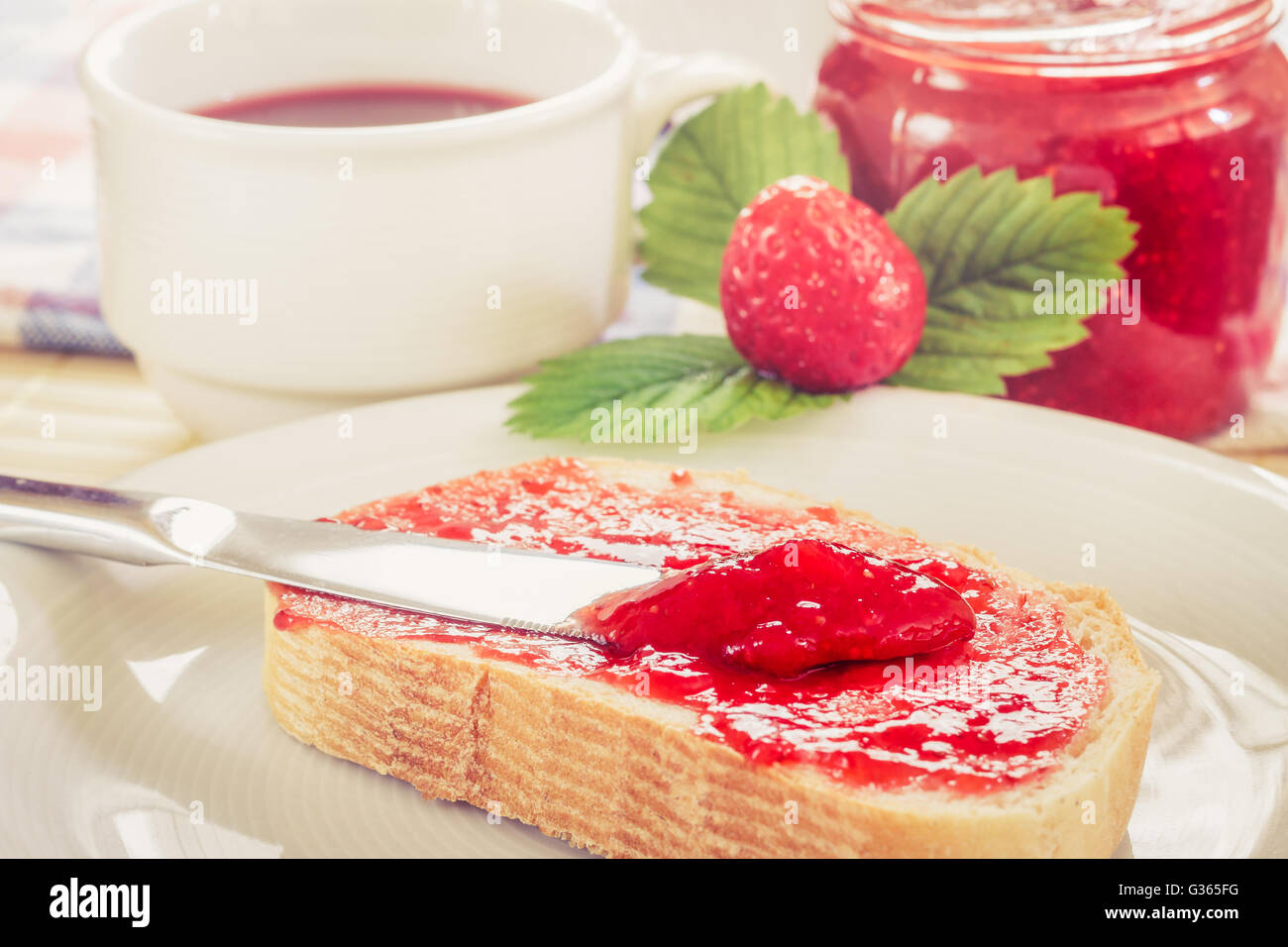 Scheibe Brot mit Glas Erdbeer Marmelade, Tee Teetasse, und frischen Erdbeeren und Blätter neben ihm. Konzept-Bild für ha Stockfoto