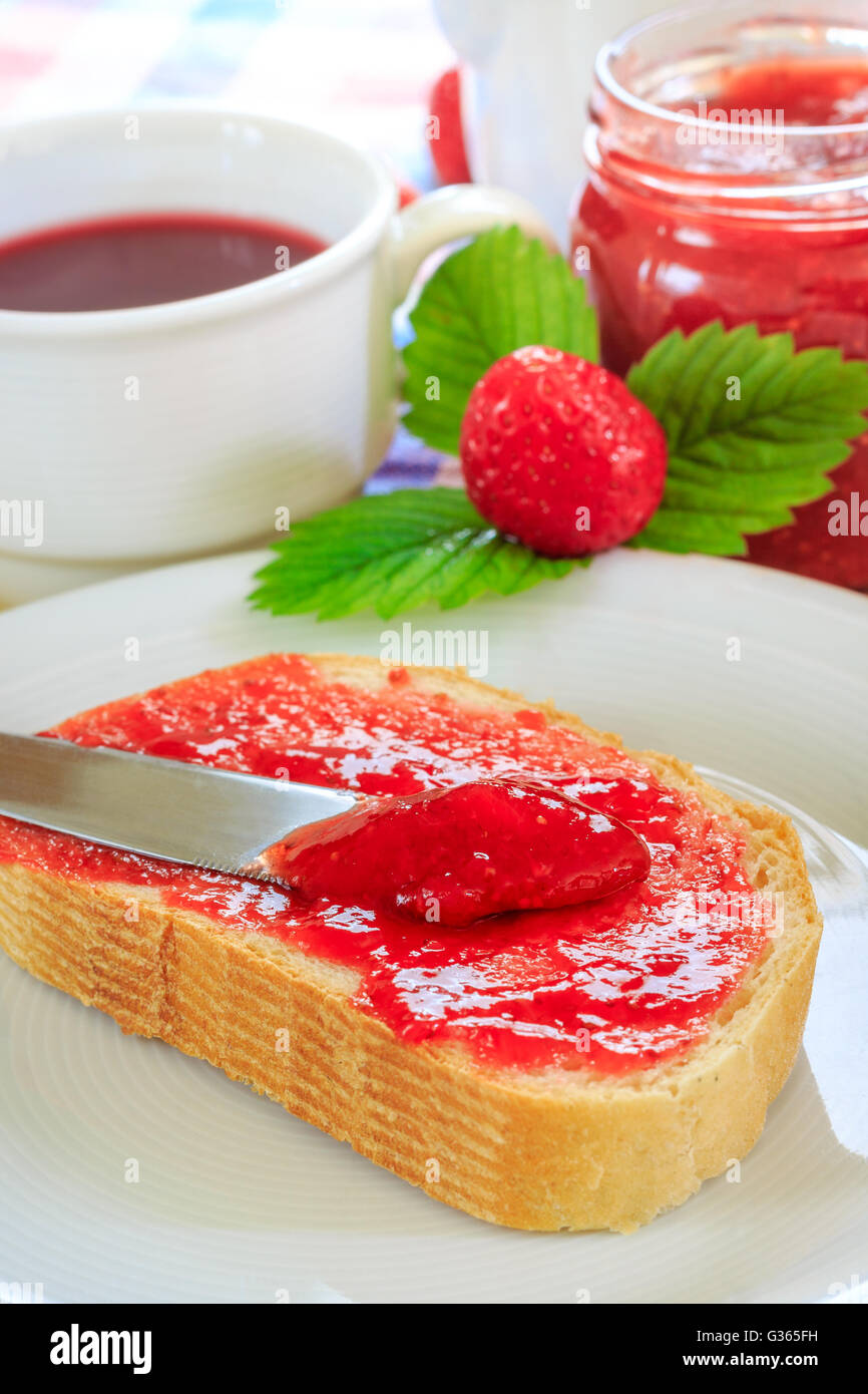 Scheibe Brot mit Glas Erdbeer Marmelade, Tee Teetasse, und frischen Erdbeeren und Blätter neben ihm. Konzept für das Frühstück Stockfoto