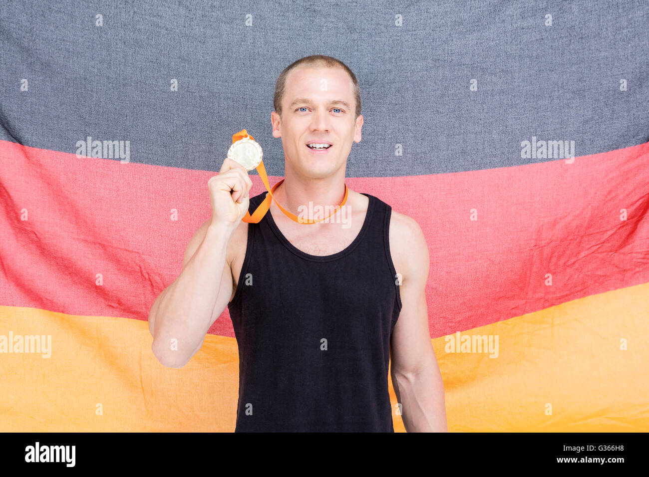 Athlet seine Goldmedaille vor deutscher Flagge zeigen Stockfoto