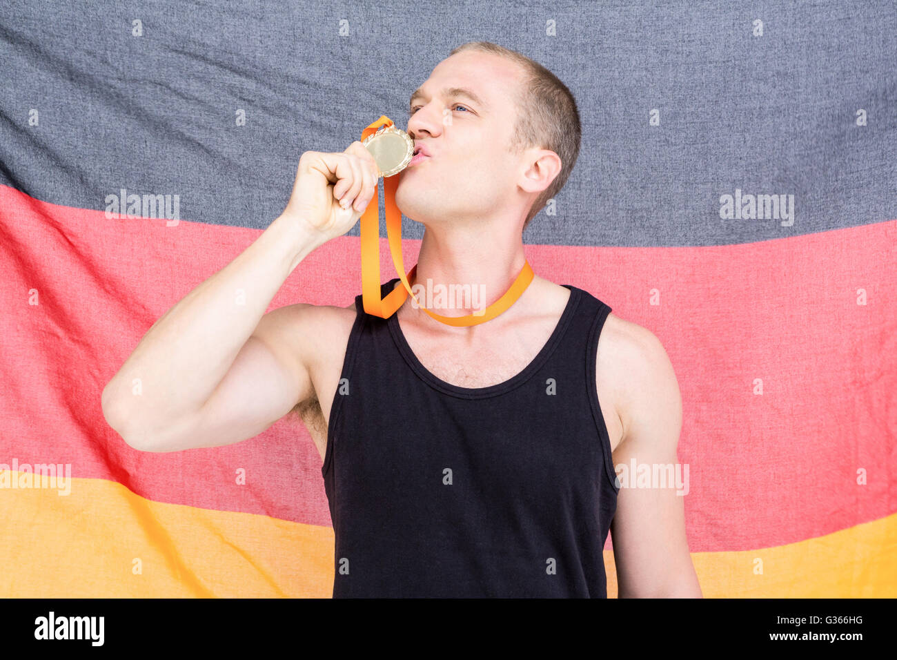 Athlet posiert mit Goldmedaille vor deutscher Flagge Stockfoto