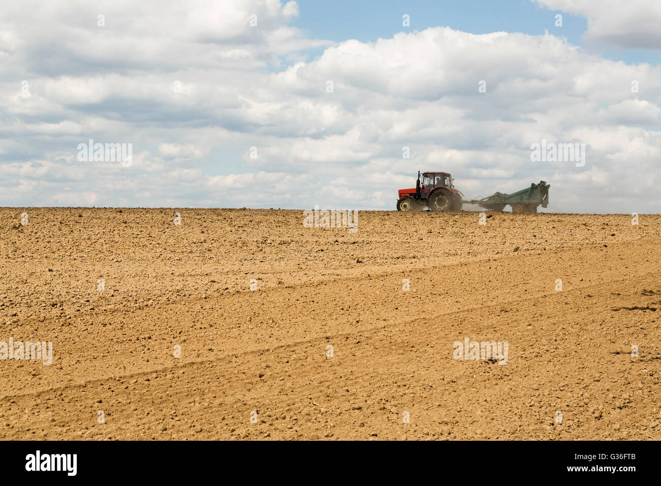 Traktor pflügen ein Feld mit einer Spur von Staub hinter sich. Blauen Himmel oben. Stockfoto