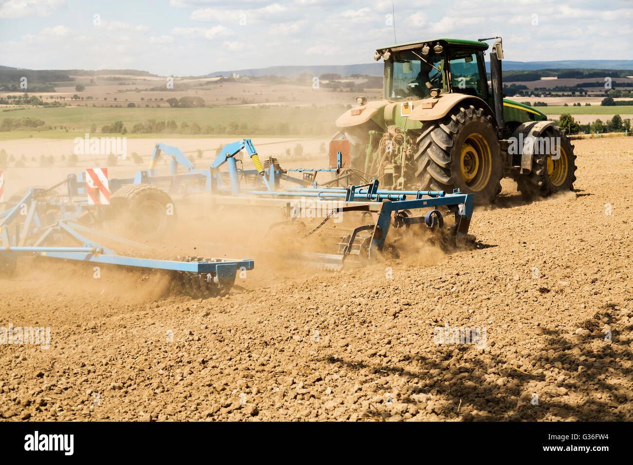 Traktor pflügen ein Feld mit einer Spur von Staub hinter sich. Stockfoto
