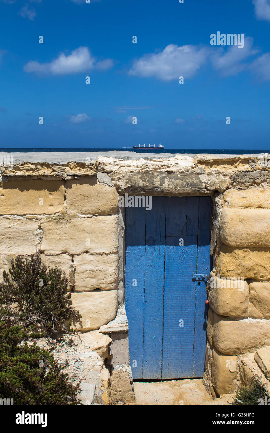 Flachbau aus Steinen mit einem blauen Holztor, farblich passend mit dem Mittelmeer im Hintergrund und einem Himmel gemacht. Groß Stockfoto
