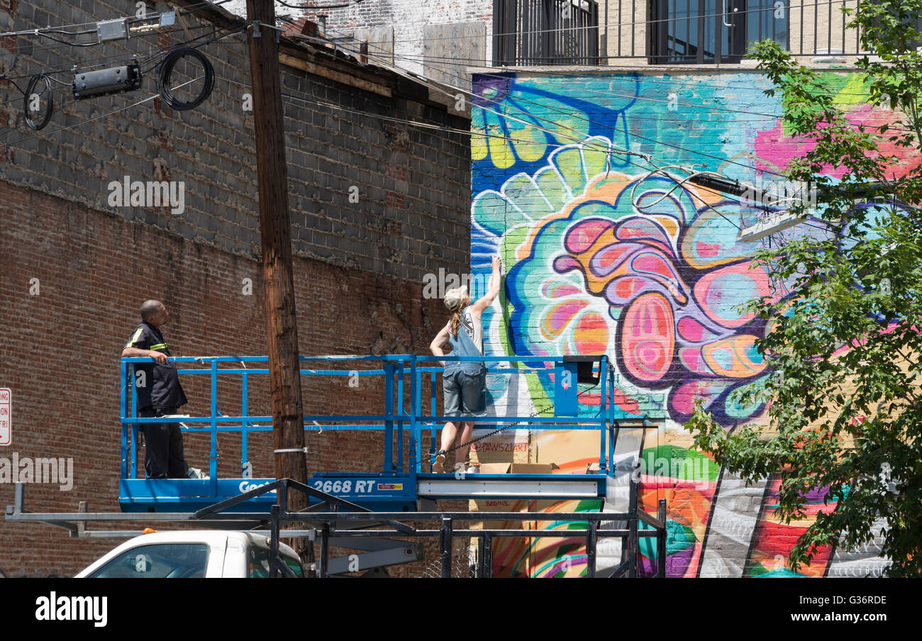 Weibliche Streetart-Künstler bei der Arbeit auf ein Wandbild auf einer erhöhten Plattform auf Christopher Columbus Drive, Jersey City Stockfoto