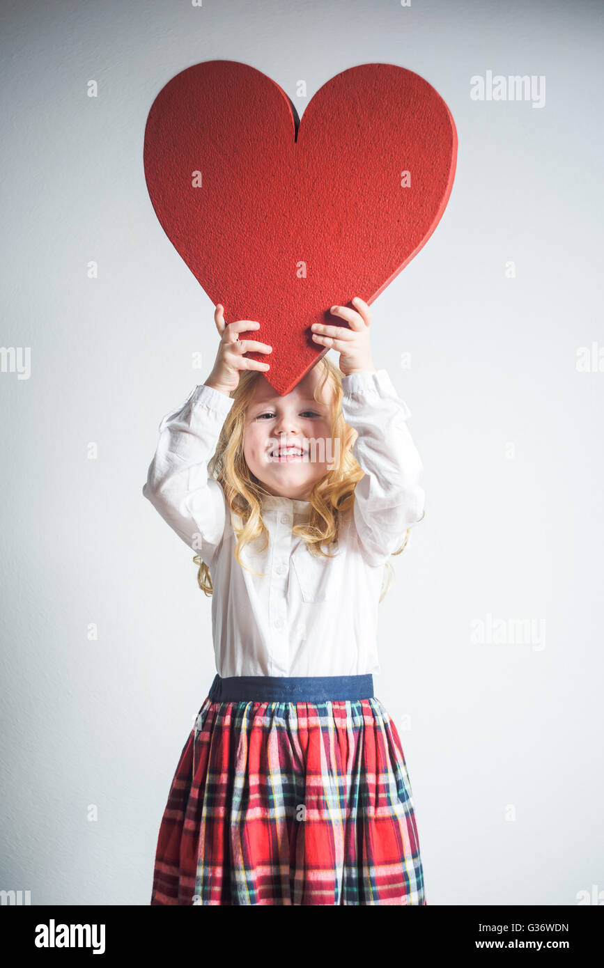 Schönen Lächeln auf den Lippen blonde Mädchen in Schuluniform mit einem großen roten Herz auf Valentinstag. Stockfoto