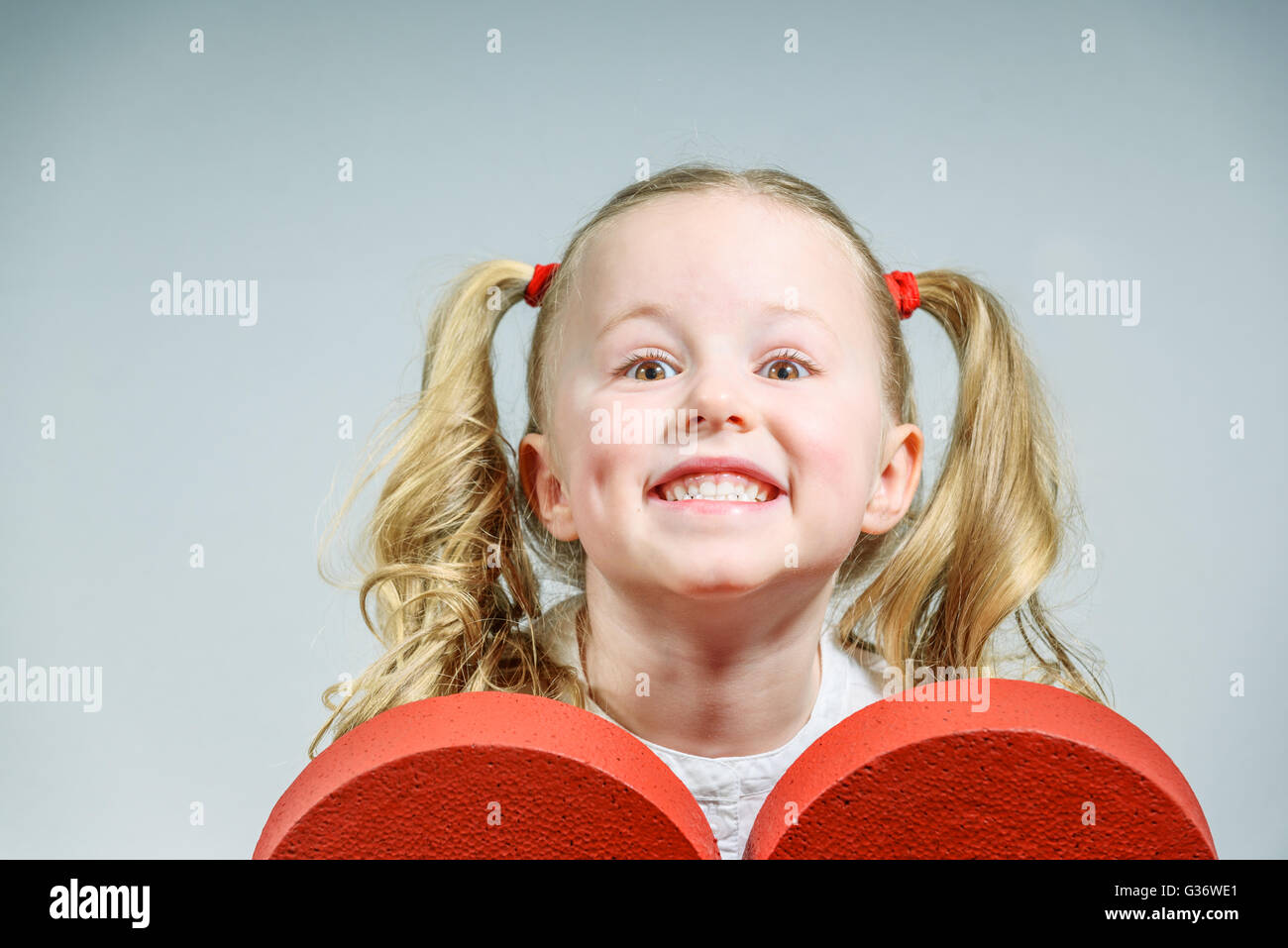 Schönen Lächeln auf den Lippen blonde Mädchen in Schuluniform mit einem großen roten Herz auf Valentinstag. Stockfoto