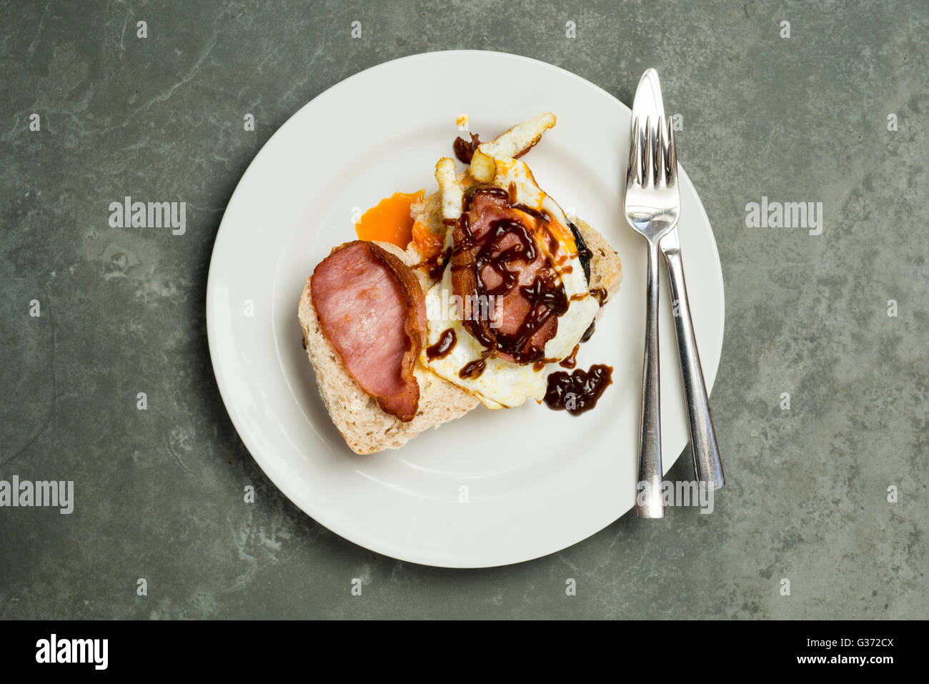 Aufwand für Speck und Ei auf Rolle mit Essgeschirr auf Teller gelegt auf eine Steinoberfläche Stockfoto