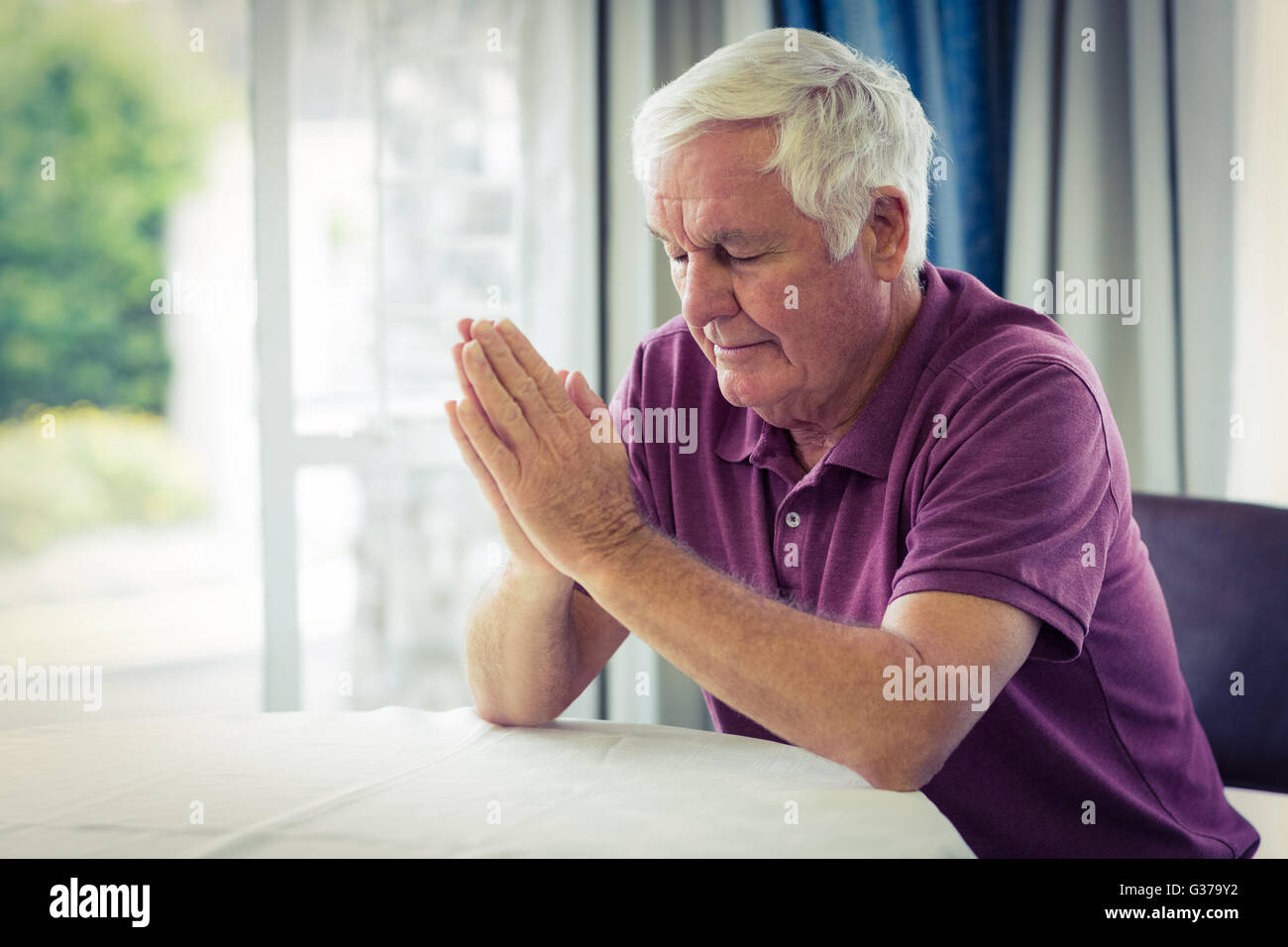 Ältere Mann, der betet im Wohnzimmer Stockfoto