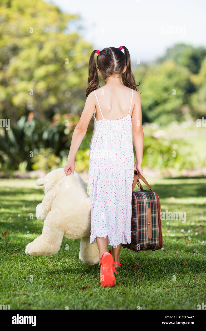 Junge Mädchen zu Fuß im Park mit einem Koffer und Teddybär Stockfoto