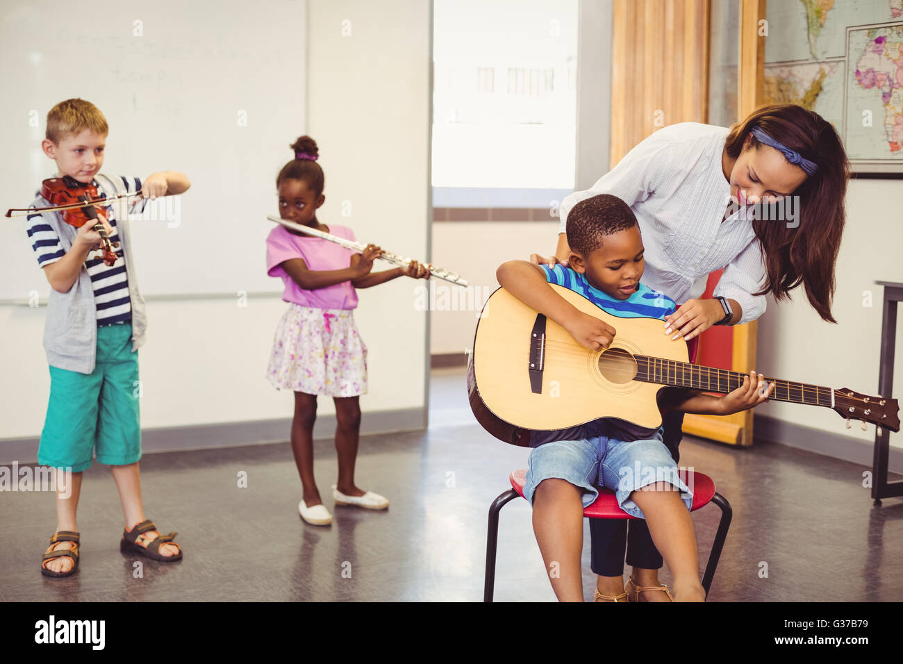 Lehrer, die Unterstützung einer Kinder zum spielen ein Musikinstrument im Klassenzimmer Stockfoto