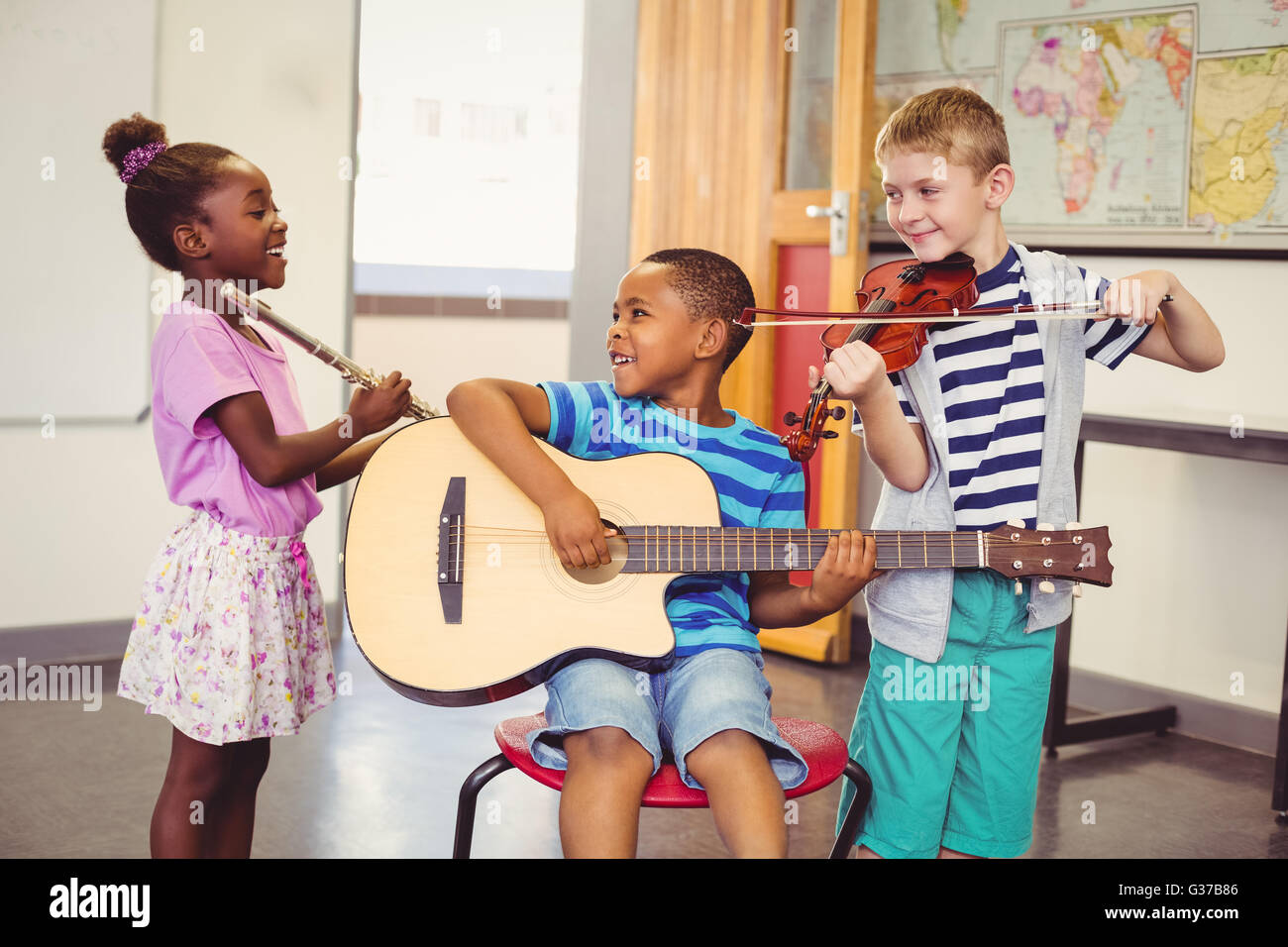 Lächelnde Kinder spielen Gitarre, Geige, Querflöte im Klassenzimmer Stockfoto