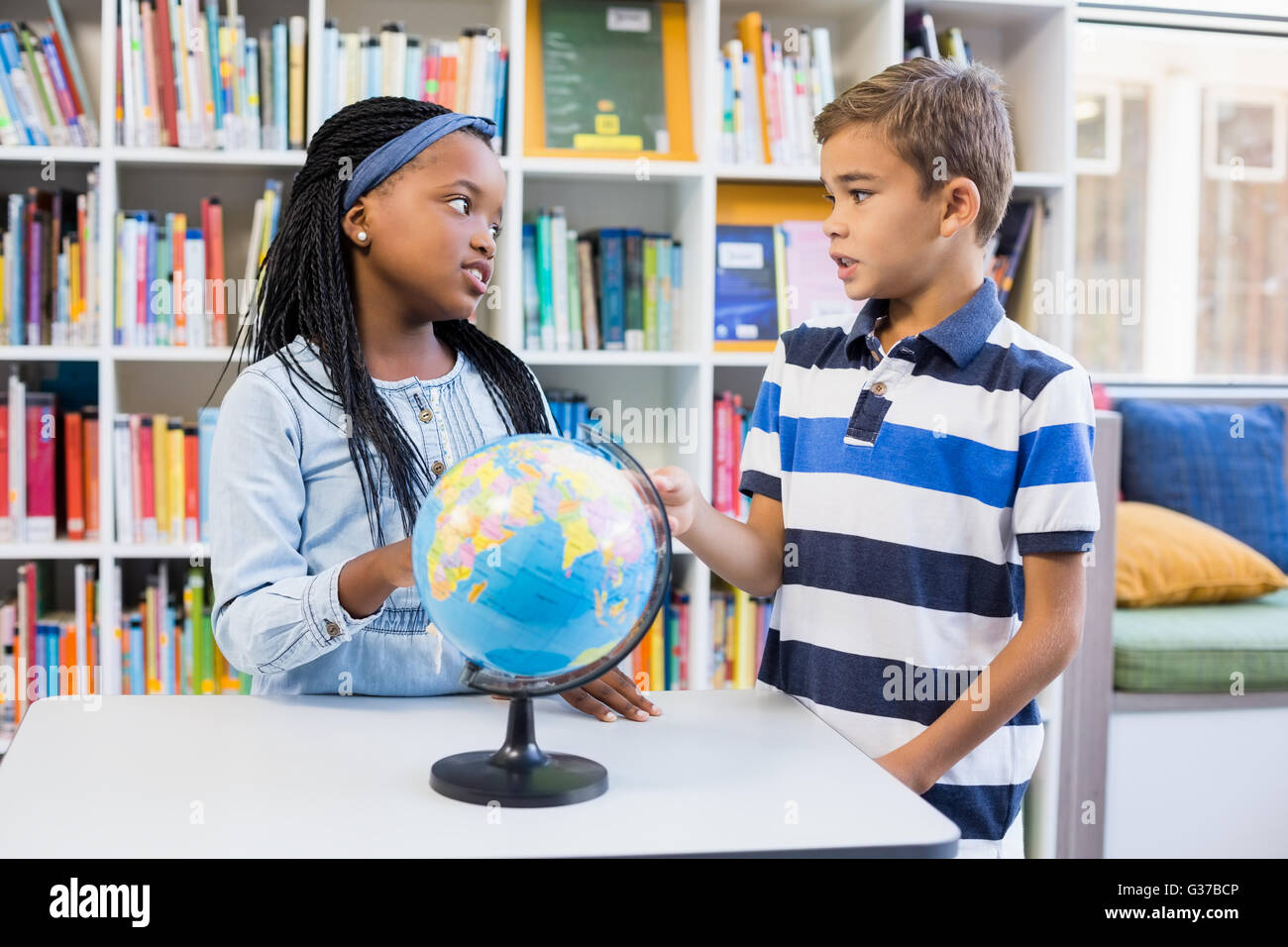 Schülerinnen und Schüler diskutieren miteinander in Bibliothek mit Globus auf Tisch Stockfoto