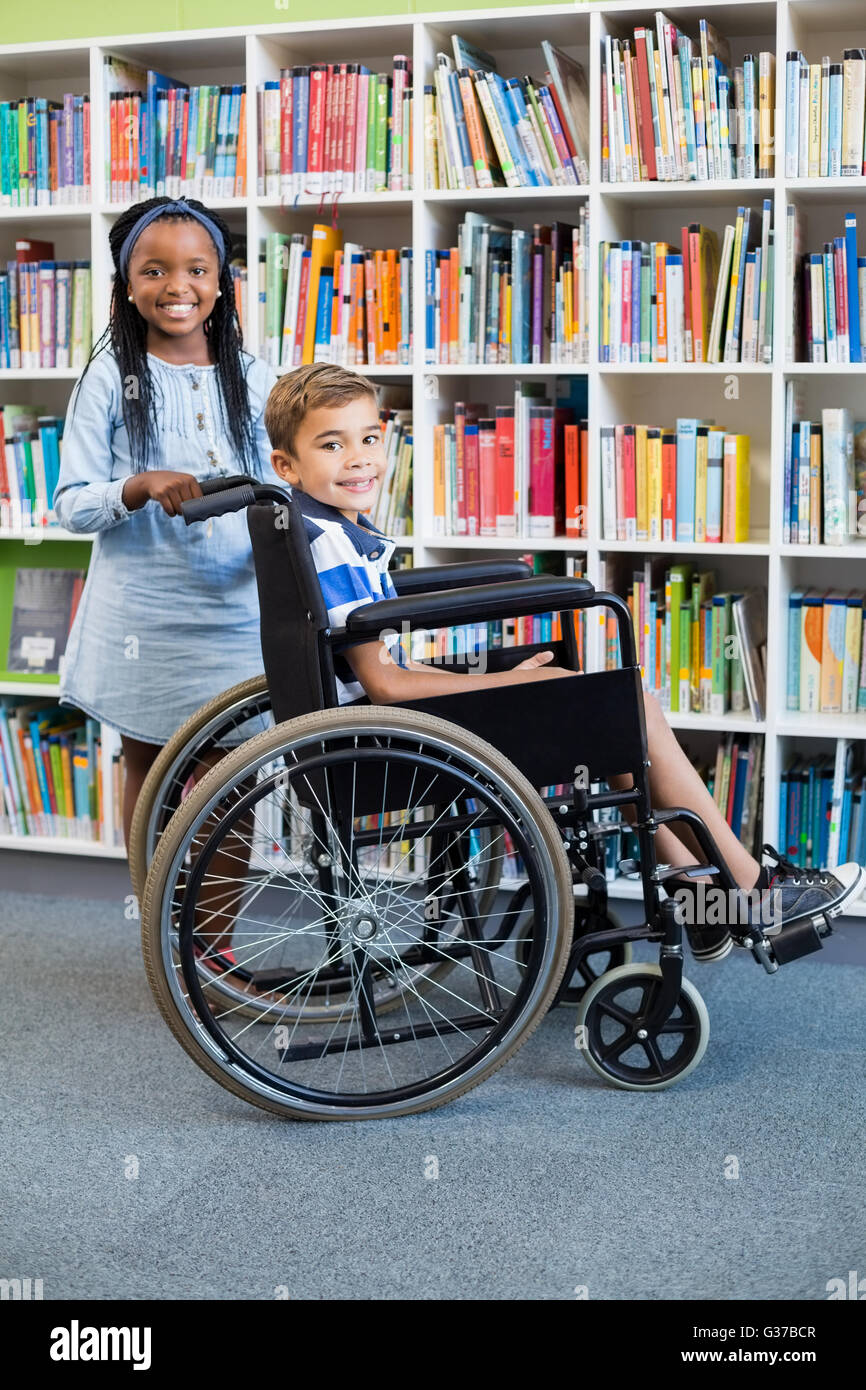 Glücklich Schulmädchen stehend mit Schuljunge auf Rollstuhl Stockfoto