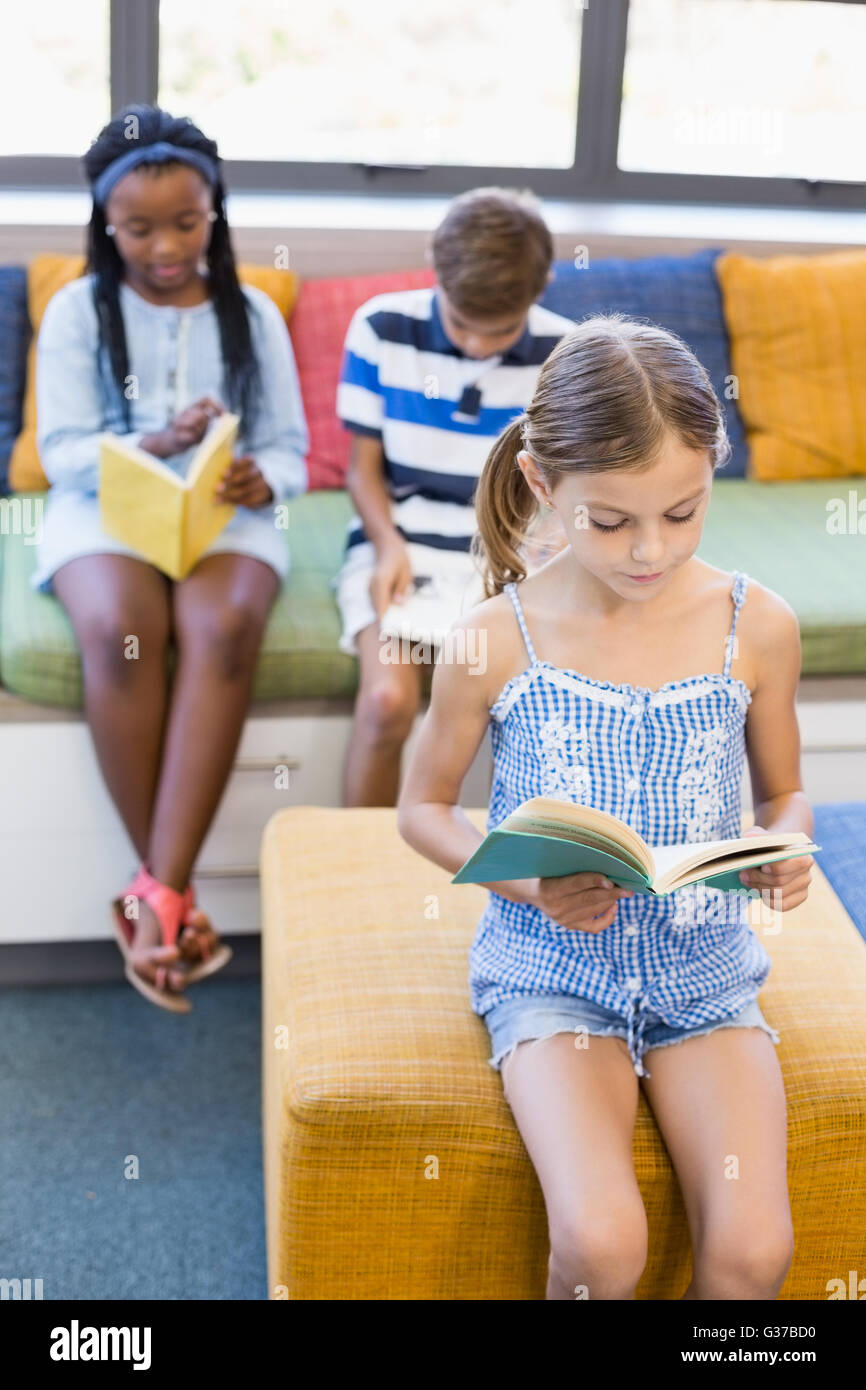 Schülerinnen und Schüler sitzen auf Sofa und Lesebuch in Bibliothek Stockfoto