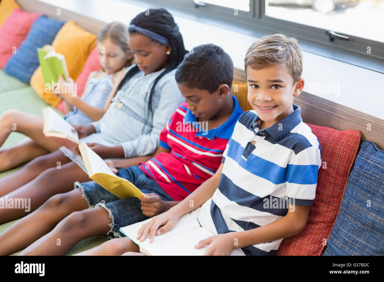 Schülerinnen und Schüler sitzen auf Sofa und Lesebuch in Bibliothek Stockfoto