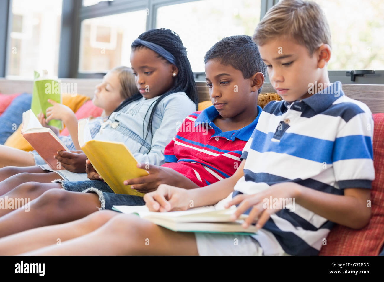 Schülerinnen und Schüler sitzen auf Sofa und Lesebuch in Bibliothek Stockfoto