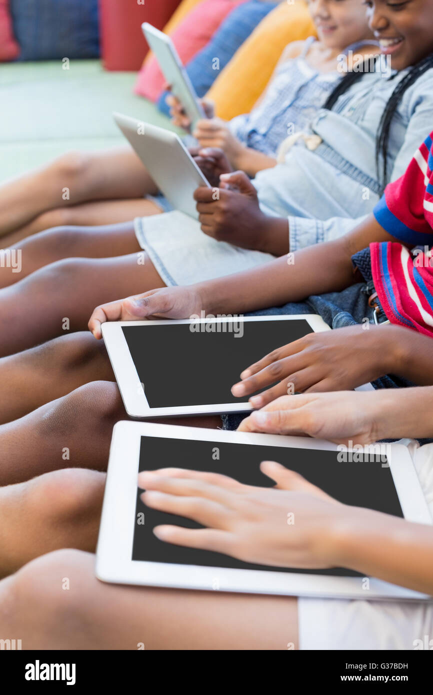 Schulkinder auf Sofa sitzen und mit digital-Tablette in Bibliothek Stockfoto