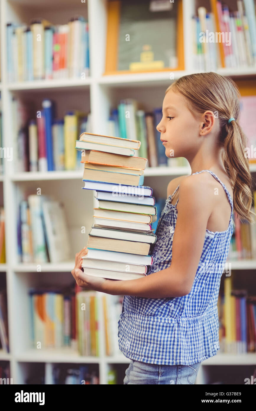 Schulmädchen hält Stapel Bücher in der Bibliothek Stockfoto